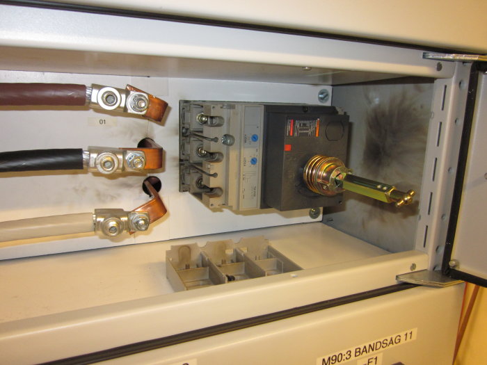Elektrisk säkerhetsbrytare med utdragen säkring och synliga skador från ett kortslutning, sot och brännskador på väggen.