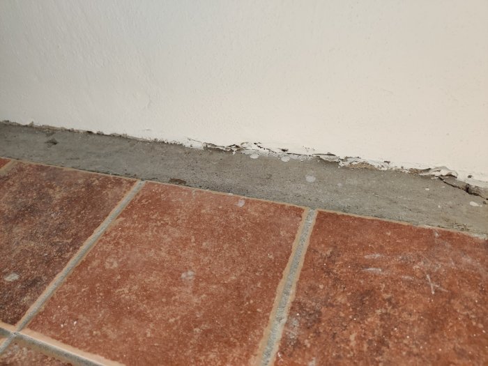 Vägg möter klinkergolv med synlig spricka och plastfolie, behöver tätas före renovering.