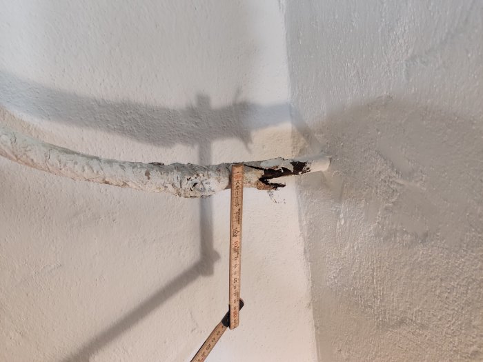 Delvis avskavt ytterhölje på servisledning med synlig metallkabel och mätstock vid vägg i renoverat källarrum.