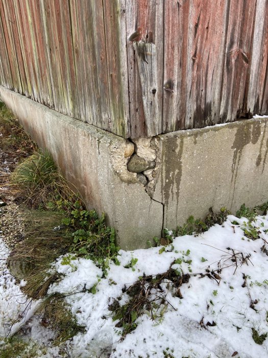 Sprucken gjuten platta och skadad stengrund vid en ladugård, med synliga sättningar vid gaveln.