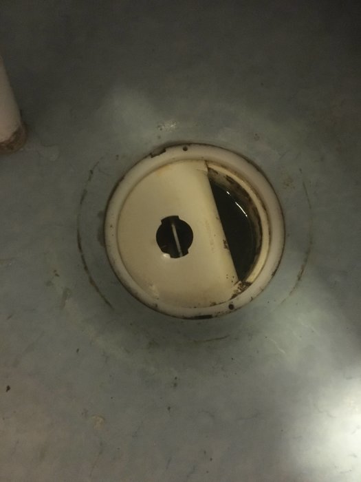 Golvbrunn med öppnat lock som visar vatten och rör, behöver eventuell rengöring.