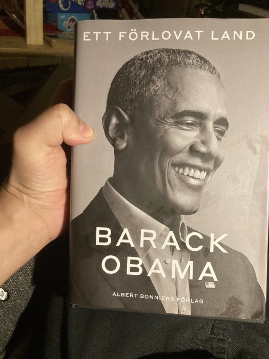 Hand håller en bok med titeln "Ett Förlovat Land" och författarnamnet "Barack Obama".