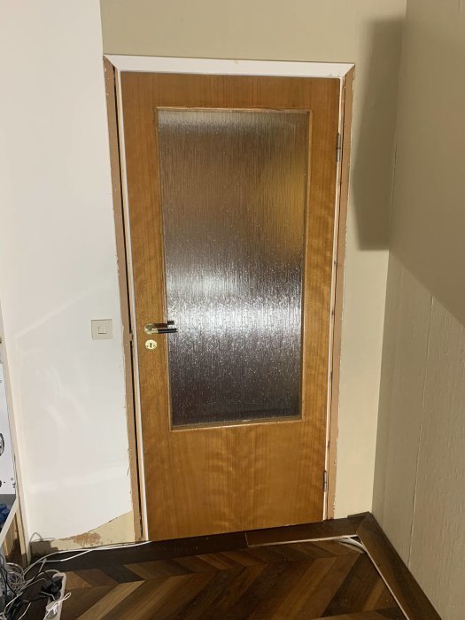 Lackad glasdörr i en hall under renovering utan dörrlister, belyst i mörkt rum.