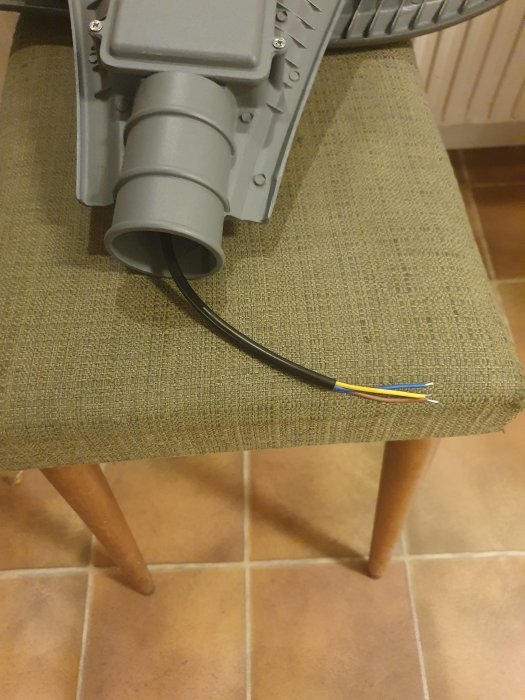 En grå kabelanslutningsbox med en svart installationskabel som sticker ut, placerad på en stol.