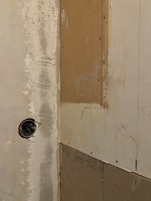 Ospacklad hörnfog med elektrisk dosa i ofärdigt kök där väggar möts, med synlig gipsskiva och spår av spackel.