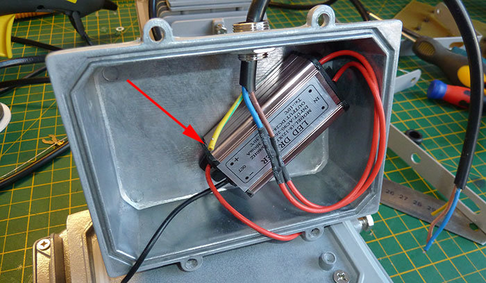 Öppen elektrisk armatur med synliga kablar och komponenter på en arbetsbänk, röd pil pekar på potentiell problemområde.