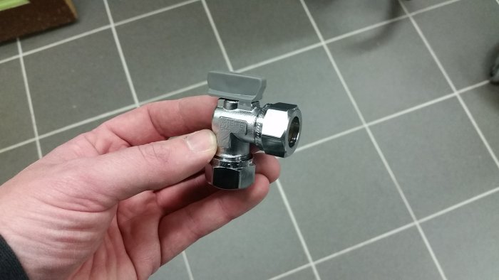 Hand håller en 15mm 90-graders kulventil av fabrikat Vatette med synligt litet genomflödeshål.