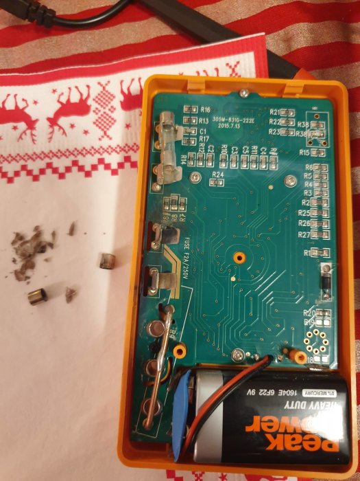 Elektronisk kretskort med en tom plats för glassäkring och glassäkringssmulor bredvid.