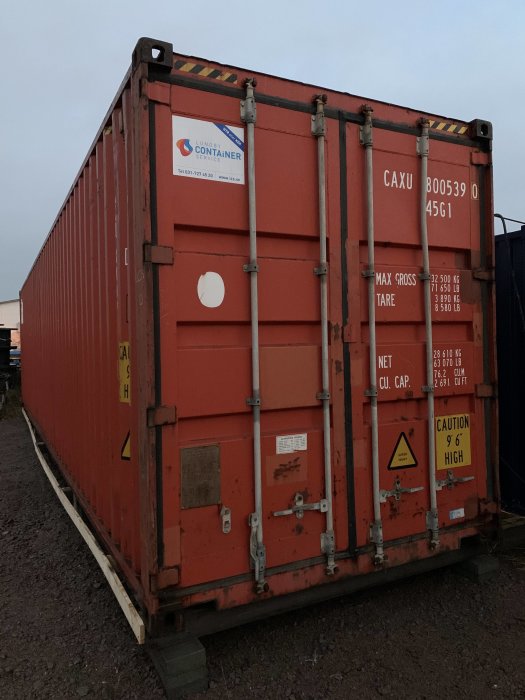 Röd 40 fots high cube shippingcontainer står på grusunderlag med företagslogotyp och lastinformation.