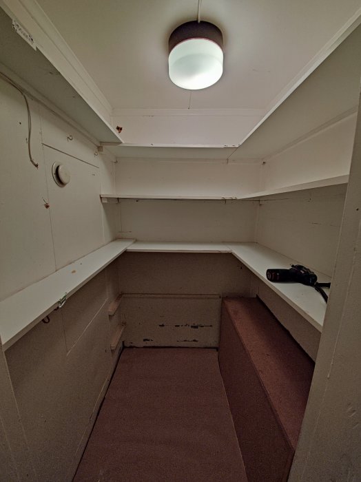 Tomt skafferi under renovering med borttagna hyllor och en borr på en hylla.