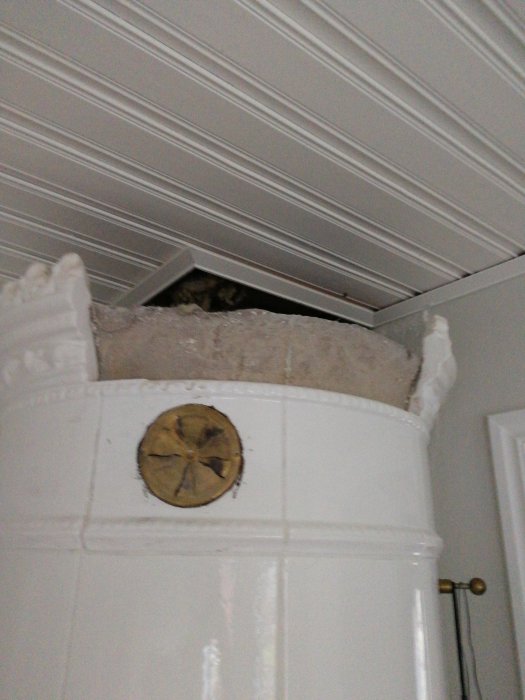 Intakt bit av kronan på en gammal kakelugn som lossnade vid målning, placerad ovanpå ugnen.