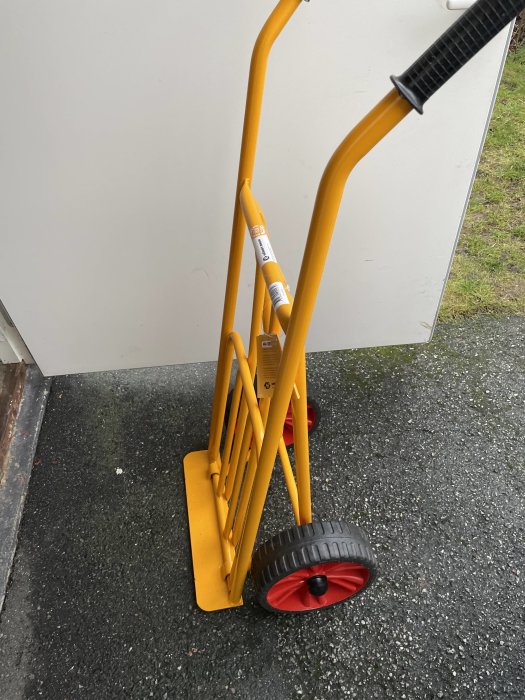 Gul handdragen sackkärra med svart handtag och rött hjul på asfalterad mark.