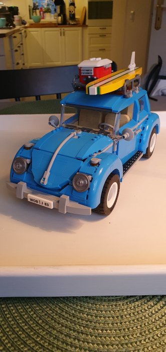 Ett färdigbyggt blått Lego Volkswagen Beetle med ett surfbräde på taket, mot köksbakgrund.