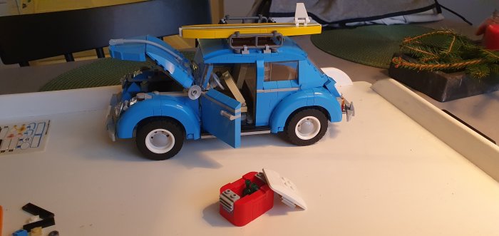 Färdigbyggt legomodell av en blå Volkswagen Typ 1 med öppet motorlock och dörrar på ett vitt bord.