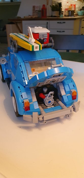 En komplett Lego-modell av en blå folkvagnsbuss med detaljer och surfbräda på taket, inomhus.