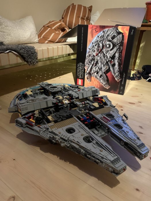 En detaljrik LEGO-modell av Millennium Falcon med dess förpackning i bakgrunden på ett trägolv.