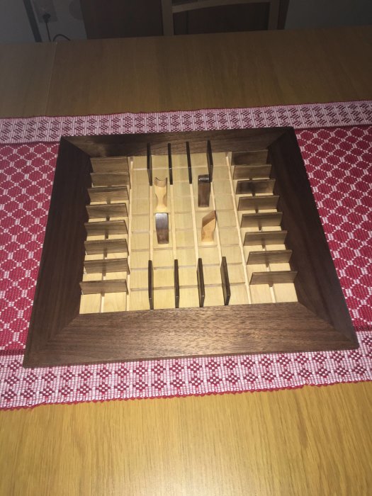 Hantverkat träspel Quoridor av ljust och mörkt trä, på ett bord med rödvit duk.