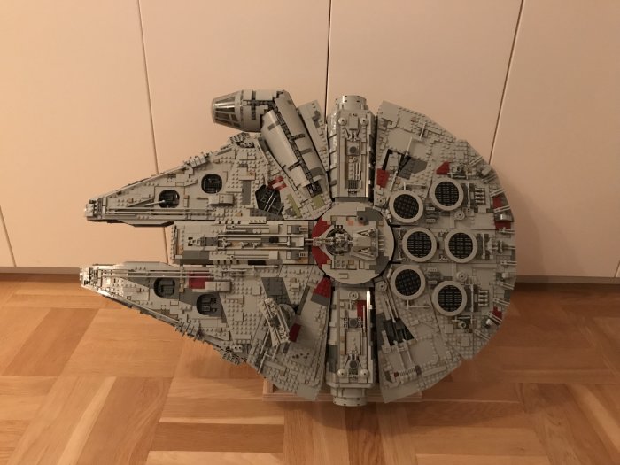 Stort Lego Star Wars Ultimate Collector's Series rymdskepp modellerat som en Millennium Falcon står på ett trägolv mot en vit vägg.