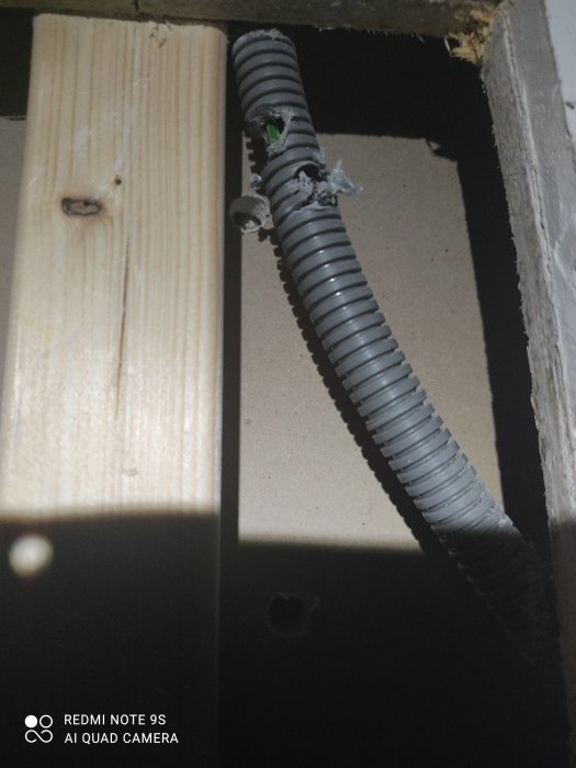 Skadat elektriskt rör i vägg med synlig kabel och borrskada.