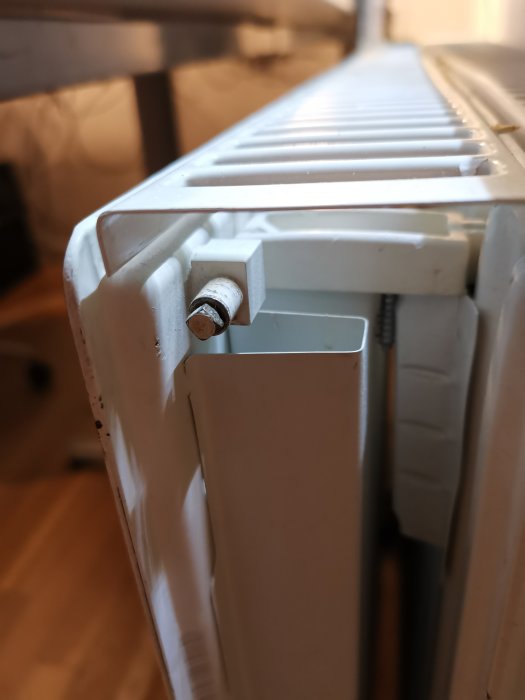 Vit radiator med en luftningsventil i översta hörnet, tecken på värmeproblem.