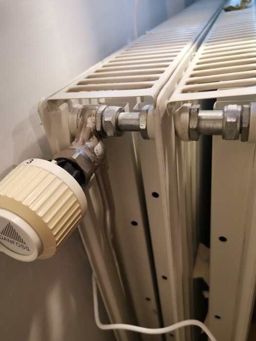 Element i hemmiljö med termostatventil från Danfoss och synliga röranslutningar.