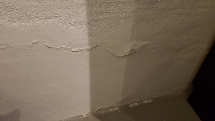 Innervägg i källare med färg som släpper och fläckar där puts behöver renoveras.