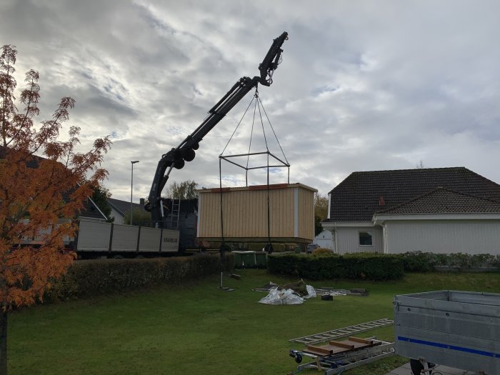 Isolerat förråd placeras på tomten med hjälp av en kranbil, mot bakgrund av ett bostadshus.