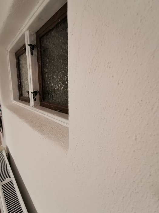 En hörnvy av en nymålad vit vägg och ett fönster med krusat glas, med synliga målarbeten kring fönsterkarmen.