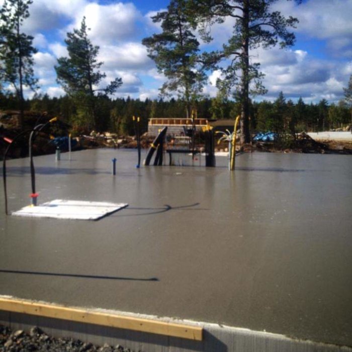 Nyligen gjuten och glättad betongplatta för husgrund med skogsbakgrund och arbetsmaterial.