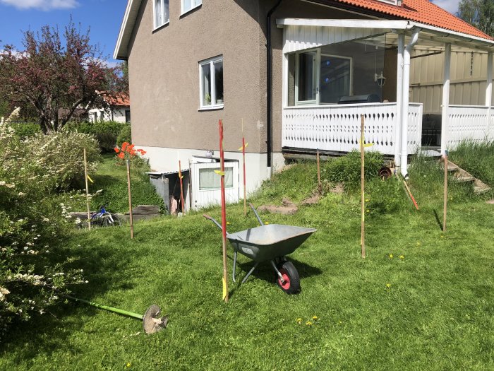 Trädgård med markerade punkter för att förbereda bygget av en ny altandel, gräsmatta och en skottkärra i förgrunden.