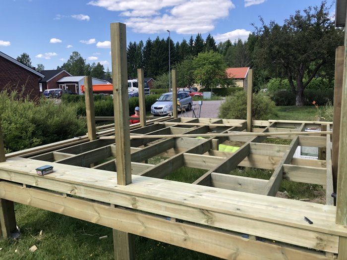 Nybyggd träram till altan med bärlinor och stolpar på plintgrund, med verktyg och hus i bakgrunden.