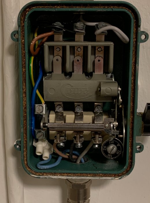 Öppet elektriskt skåp med en gammal trefasbrytare, ledningar anslutna till terminaler, installationsdetaljer synliga.