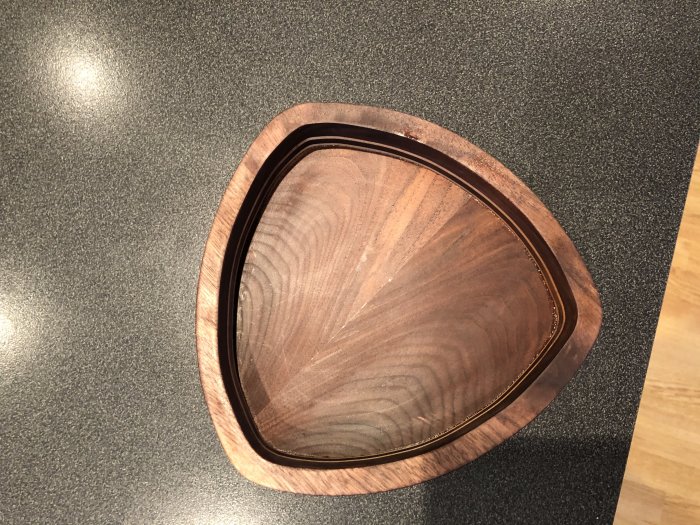 Trekantig skål i mörkt valnötsträ med ljusare lönnkantsdetaljer på en köksbänk.