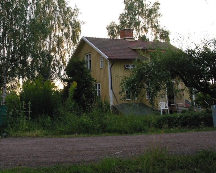 Ett gult trähus från 1912 inramat av grönska, i skymningen, med synliga tecken på förfall.