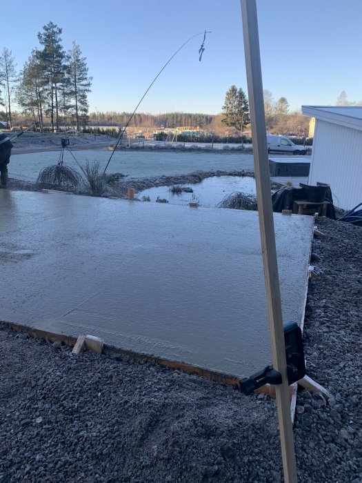 Nyligen gjuten betongplatta med träramar på en byggplats, med skog och frostig mark i bakgrunden.