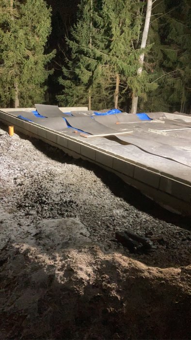 Nyutgjuten betongplatta täckt med värmemattor på natten i kallt väder, omgiven av mörk skog.