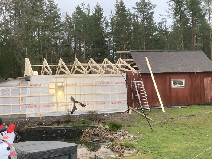 Nyinstallerade saxtakstolar på en byggnad under konstruktion, täckt av presenning, med stege framför.