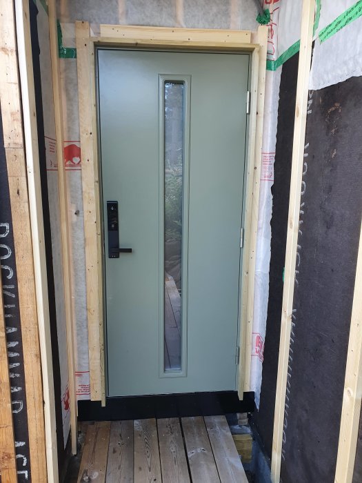 Nyinstallerad modern dörr med sidofönster i en byggkonstruktion med isoleringsmaterial och reglar synlig.