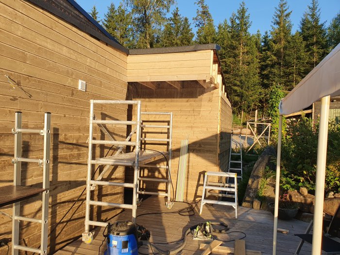 Renoveringsarbete på hus med ny panel och kröningsplåt på taket, byggställningar och verktyg syns.
