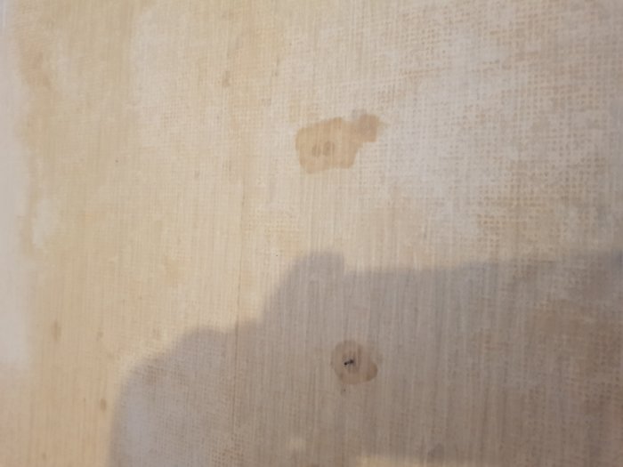 Vägg med fuktmärken och tapetrester i ett rum där renovering påbörjats.