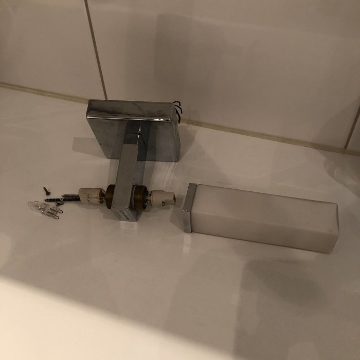 Vägglampa med en glasskärm som sitter på och en som saknas, på badrumsfliser.