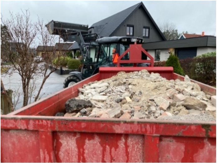 Lastbil fyller container med rivningsavfall från husrenovering.