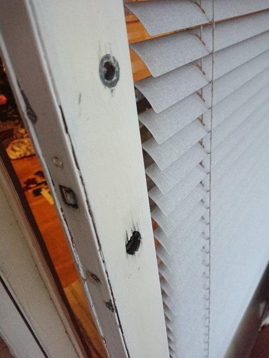 Närbild på dörrkarmens insida med synliga låshål och en vit persienn i bakgrunden.