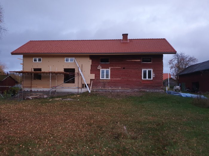 Hus under fasadrenovering med en del isoleringsskivor uppsatta och ställningar, mot bakgrund av en mulen himmel.