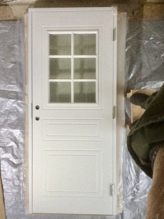 Ny vit ytterdörr med spröjsade fönster och paneler, liggande på golvet.