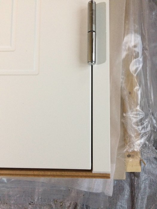 Närbild av en ny vit ytterdörr med gångjärn och en trätröskel, skyddad av plastfilm.