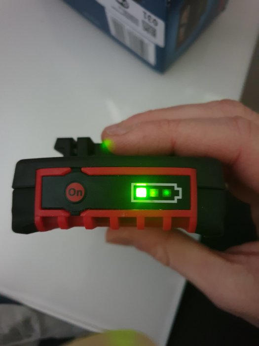 Hand håller ett nytt 18v 2ah Bosch batteri med laddindikatorn tänd.
