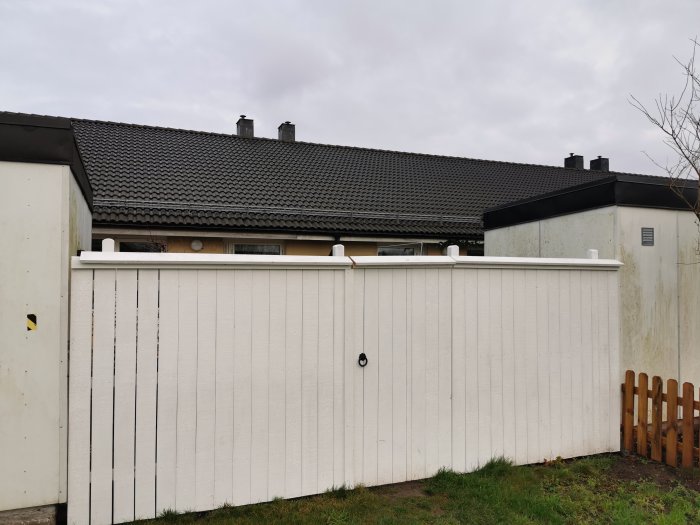 Vit staket framför hus med taktegel och skorstenar, med en liten trägrind.