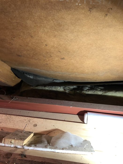 Insyn på vinden med synligt skadad vindpapp och isolering samt trälister och elrör.