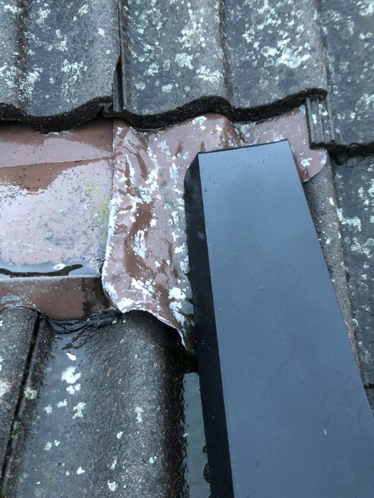 Detaljbild på tak med takpannor och plåtarbete, inklusive en förskjuten takpanna och flexibelt plåtsegment.